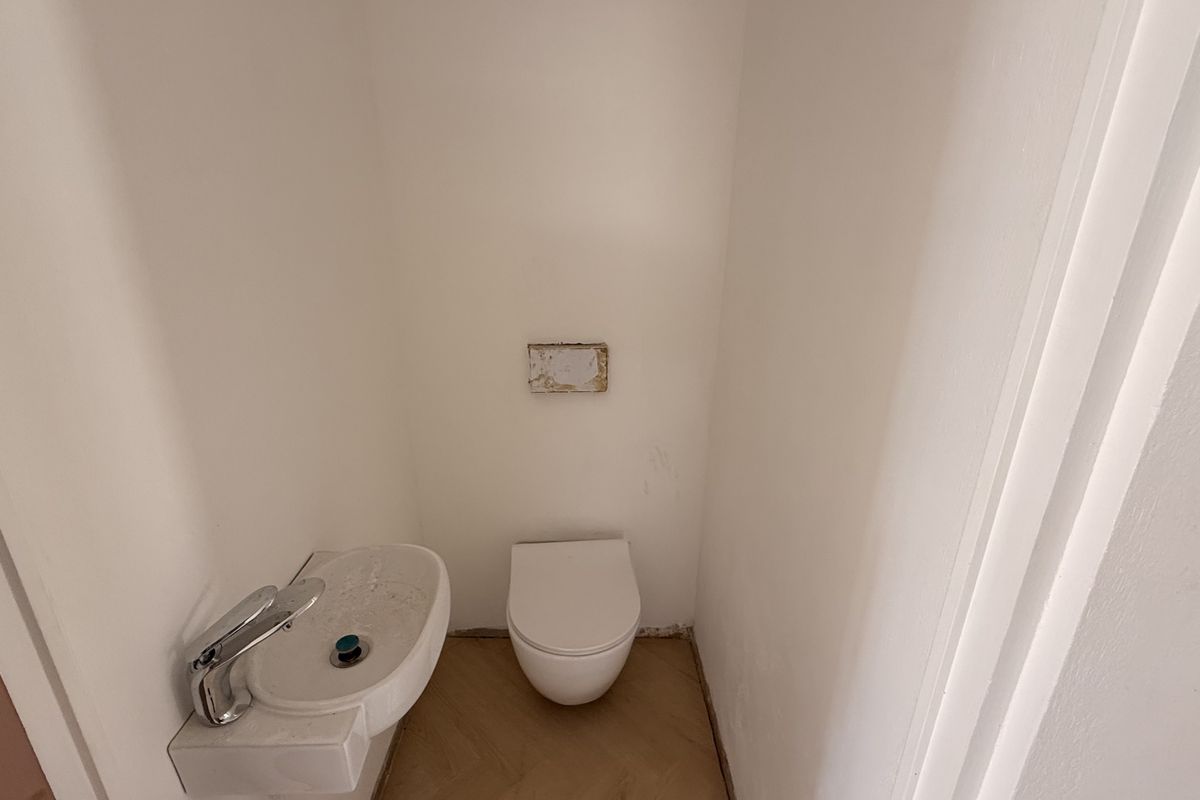 A small, minimalist powder room featuring a wall-mounted toilet and basin, currently requiring minor finishing touches to the floor and wall fixtures.
