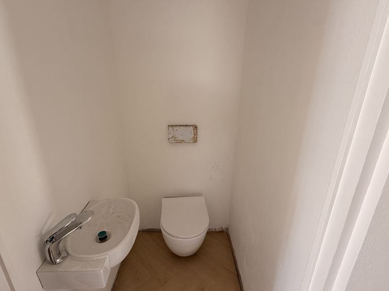 A small, minimalist powder room featuring a wall-mounted toilet and basin, currently requiring minor finishing touches to the floor and wall fixtures.