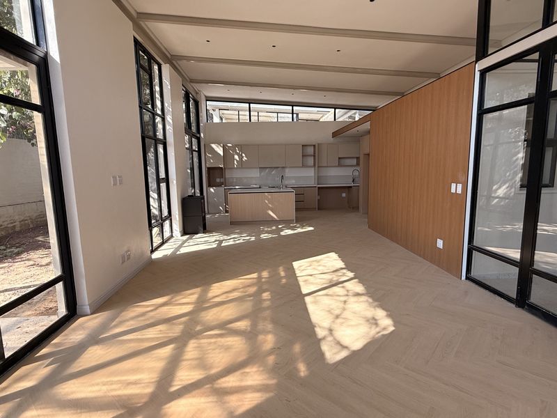 Spacious open-plan living and kitchen area featuring modern herringbone timber flooring, floor-to-ceiling black steel-framed windows, and sleek built-in cabinetry.