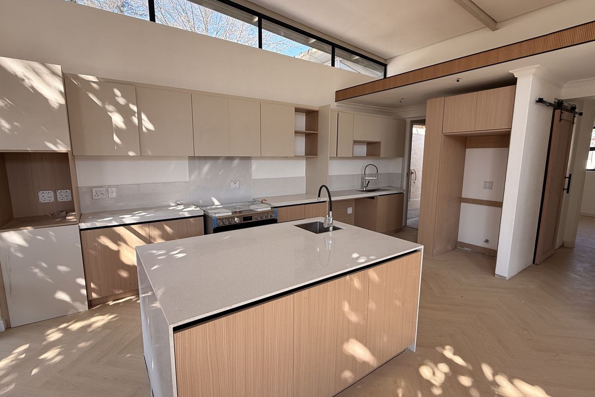 Modern kitchen featuring light wood cabinetry, quartz countertops, a central island with sink, herringbone flooring, and high clerestory windows for natural light.