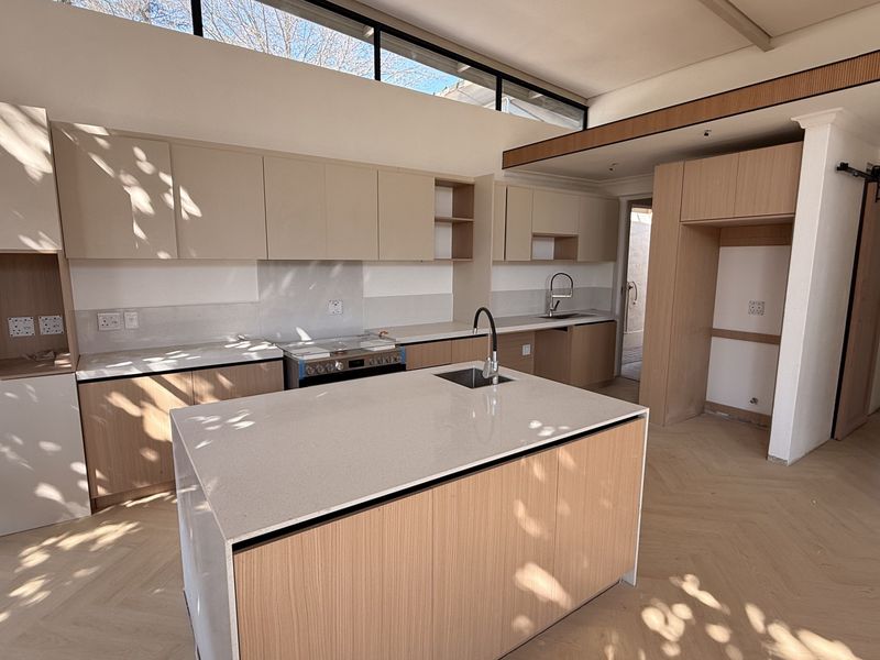 Modern kitchen featuring light wood cabinetry, quartz countertops, a central island with sink, herringbone flooring, and high clerestory windows for natural light.