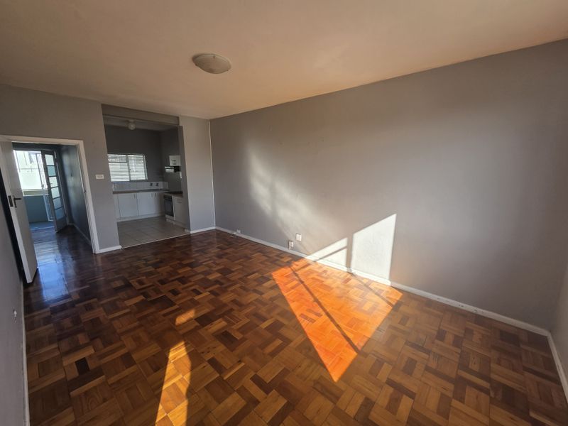An open-plan living area featuring traditional parquet flooring, leading into a functional kitchen space with built-in cabinetry and appliances.