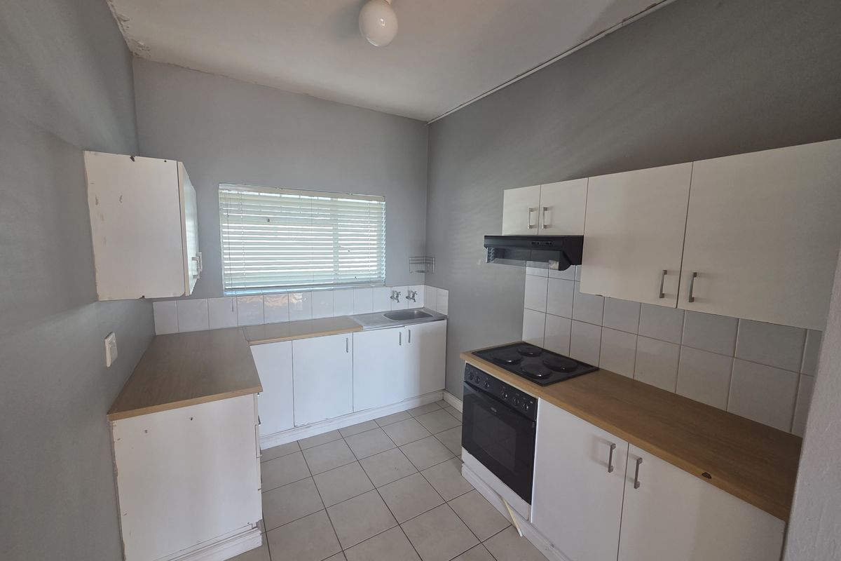 A functional kitchen featuring white cabinetry, laminate countertops, built-in oven and hob, tiled splashbacks, and tiled flooring.