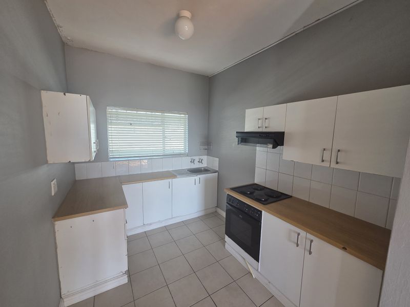 A functional kitchen featuring white cabinetry, laminate countertops, built-in oven and hob, tiled splashbacks, and tiled flooring.