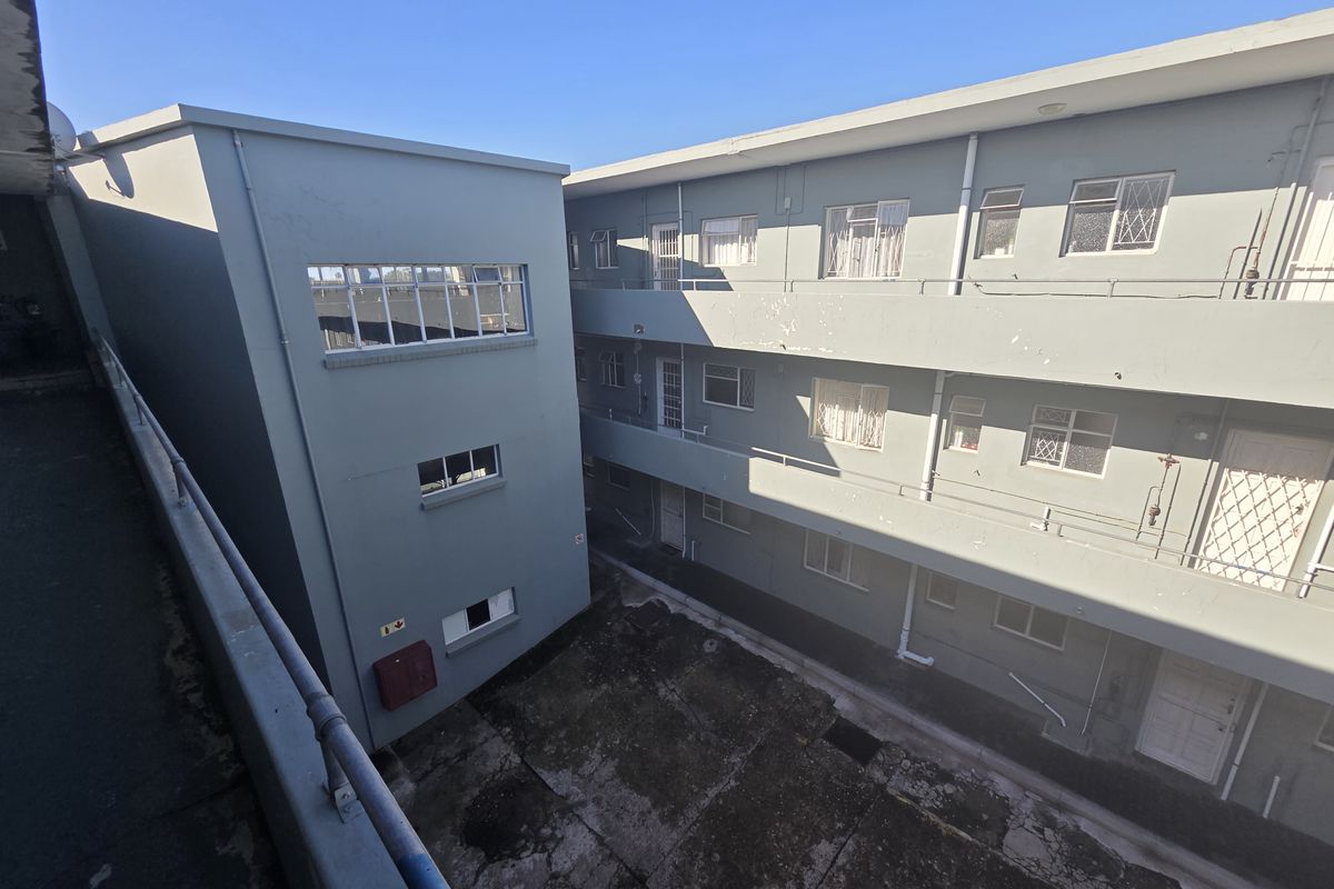 Exterior view of an apartment complex courtyard featuring concrete walkways, metal railings, and multi-level residential access points.