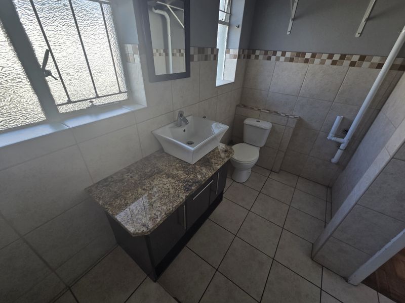 A functional bathroom featuring a granite-topped vanity with a vessel sink, tiled finishes, and a standard toilet.