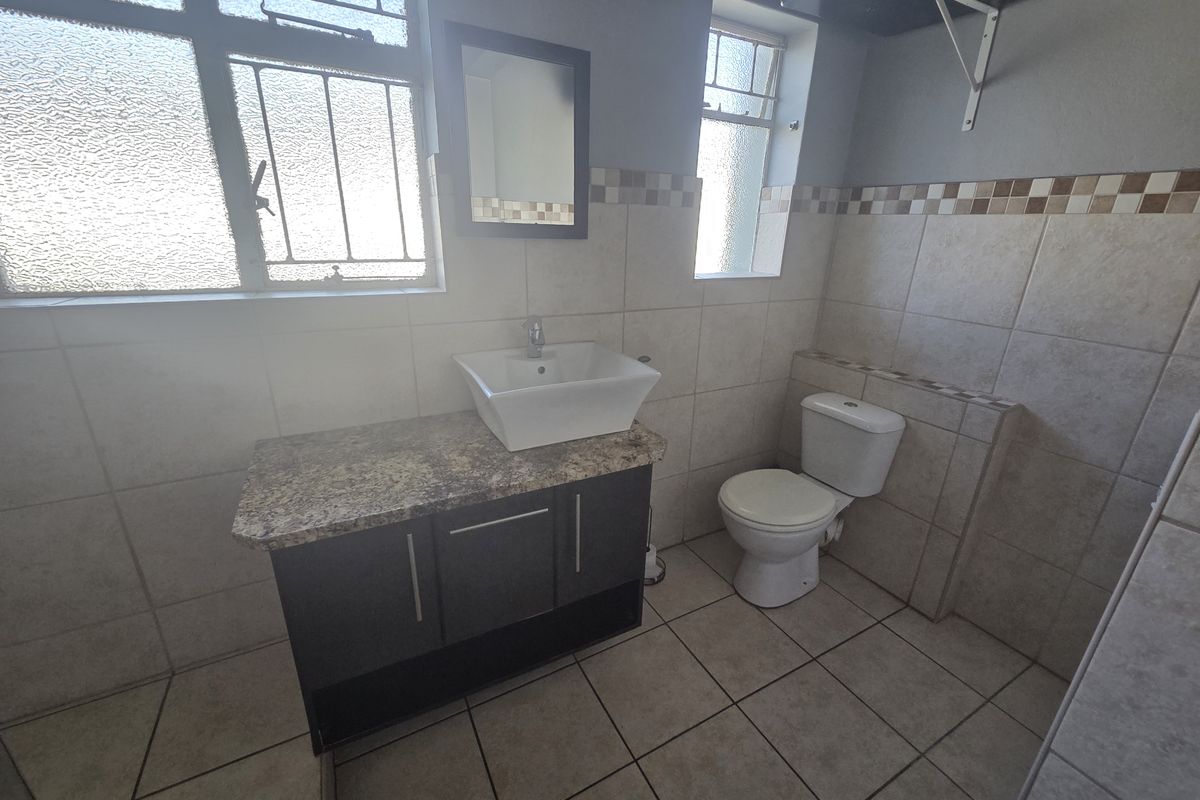 A functional bathroom featuring a vanity cabinet with a granite countertop, vessel sink, toilet, and neutral wall and floor tiling.