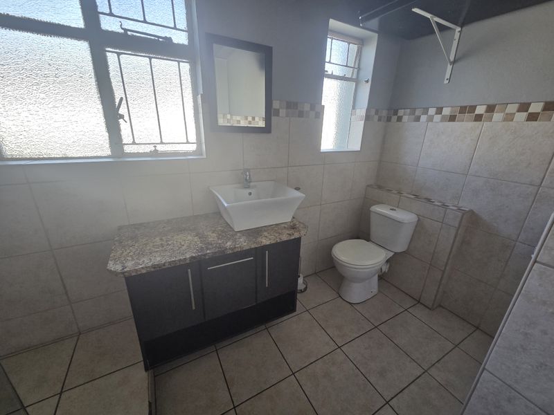 A functional bathroom featuring a vanity cabinet with a granite countertop, vessel sink, toilet, and neutral wall and floor tiling.