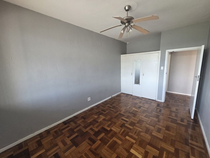A vacant bedroom featuring classic parquet flooring, a built-in wardrobe, and a ceiling fan, offering a neutral canvas for personalization.