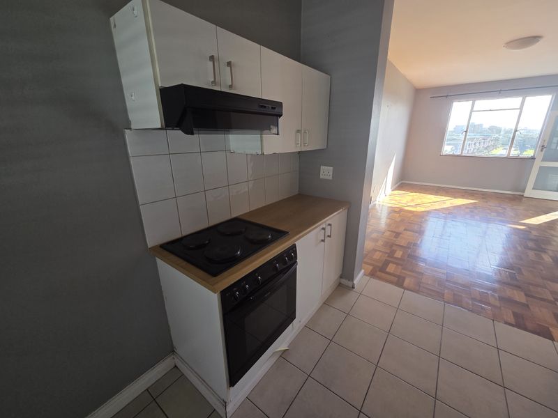 Open-plan kitchen and living area featuring parquet flooring, tiled kitchen zone, and built-in cabinetry with an integrated stove and extractor fan.