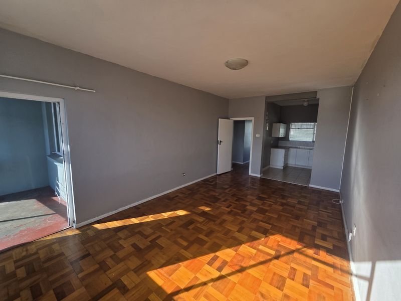 Spacious open-plan living area featuring classic parquet flooring, leading into a functional kitchen space with built-in cabinetry.