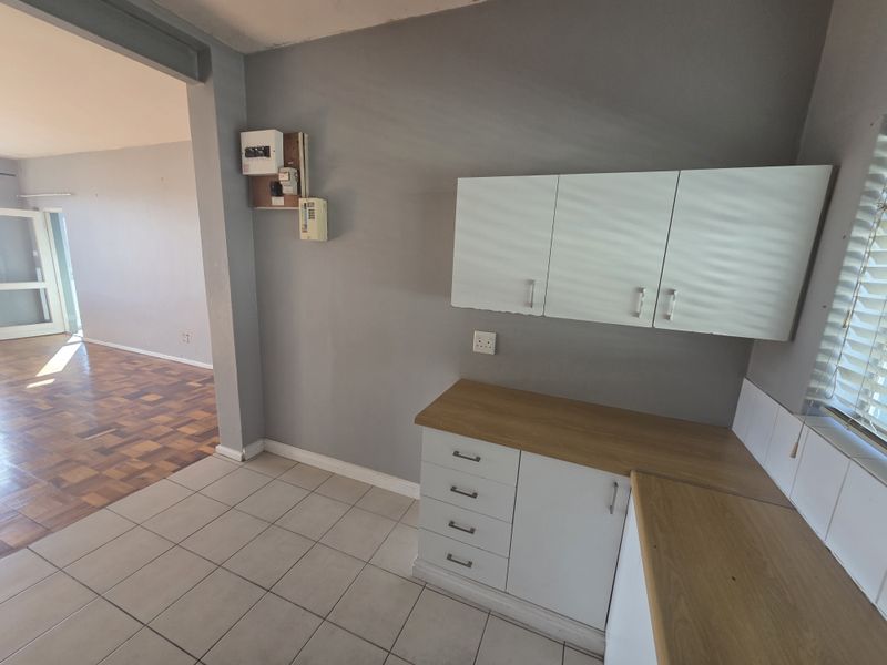 A functional kitchen area featuring built-in white cabinetry, wood-look laminate countertops, tiled flooring, and an adjacent open-plan living space with parquet flooring.