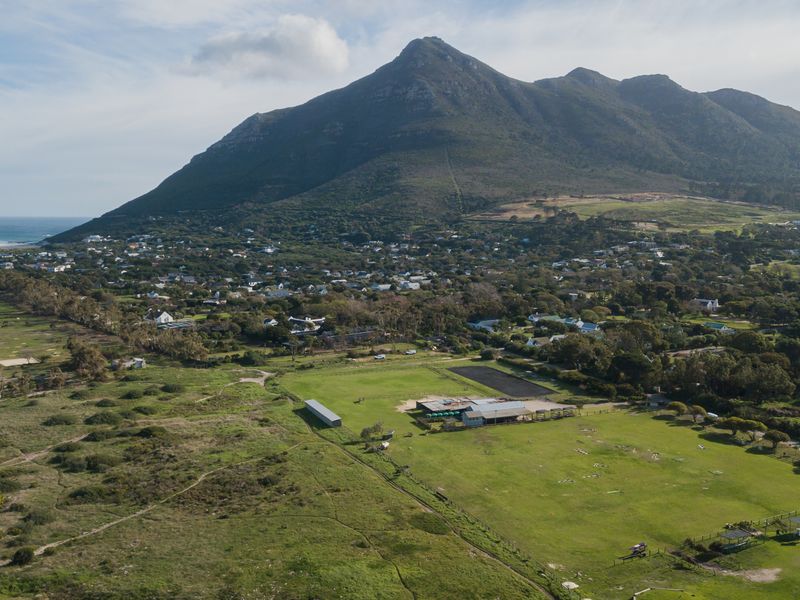 An aerial view of a large residential vacant land plot featuring open pasture, perimeter fencing, and existing outbuildings set against a mountain backdrop.