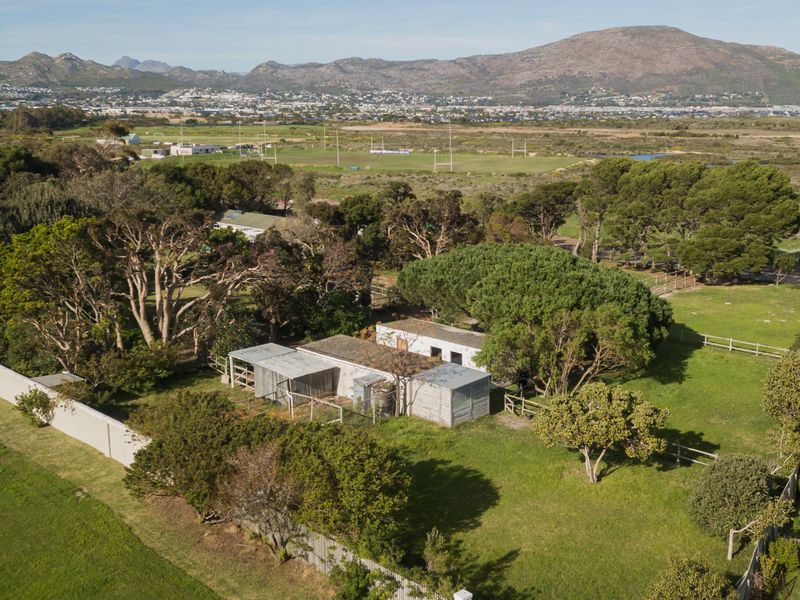 Aerial view of a residential land plot featuring existing outbuildings, mature trees, and perimeter fencing with expansive mountain and landscape views.