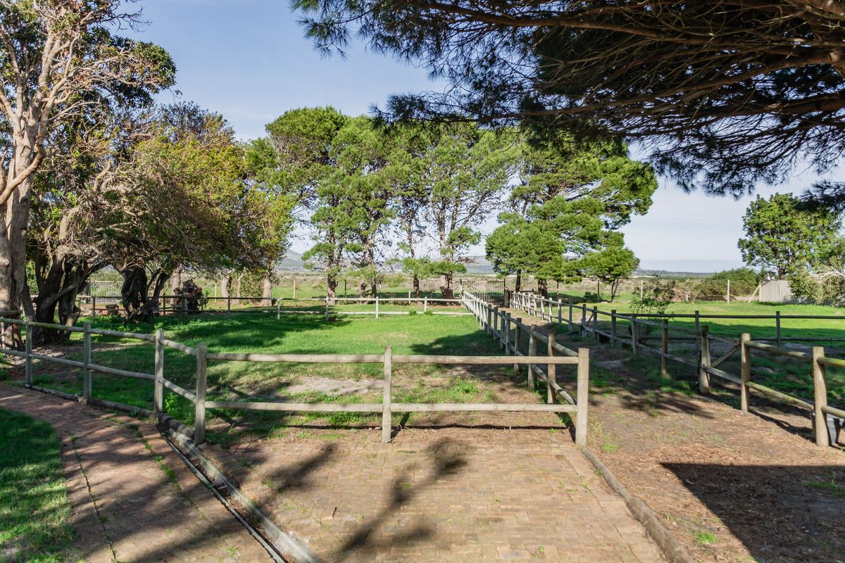 A well-maintained residential garden featuring a brick paved pathway, established mature trees, and timber post and rail fencing enclosing a grass lawn.