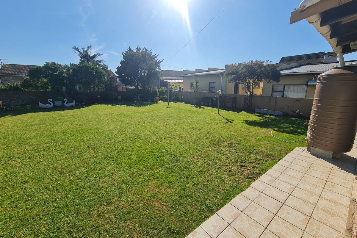 A spacious rear garden featuring a well-maintained lawn, a tiled patio area, and a water storage tank against the boundary wall.