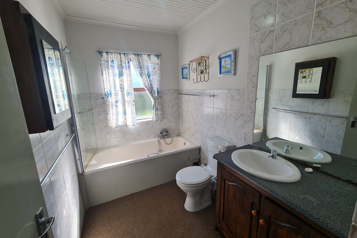 A functional bathroom featuring a built-in vanity, bathtub with shower screen, and wall tiling. The space would benefit from modern updates to finishes.