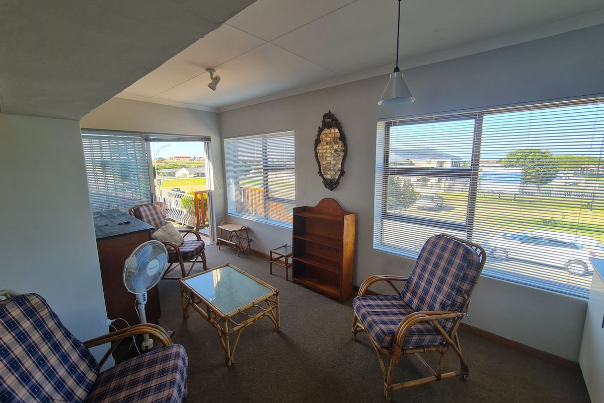 A sunlit living area featuring large windows with blinds, carpeted flooring, and direct access to an outdoor balcony space.
