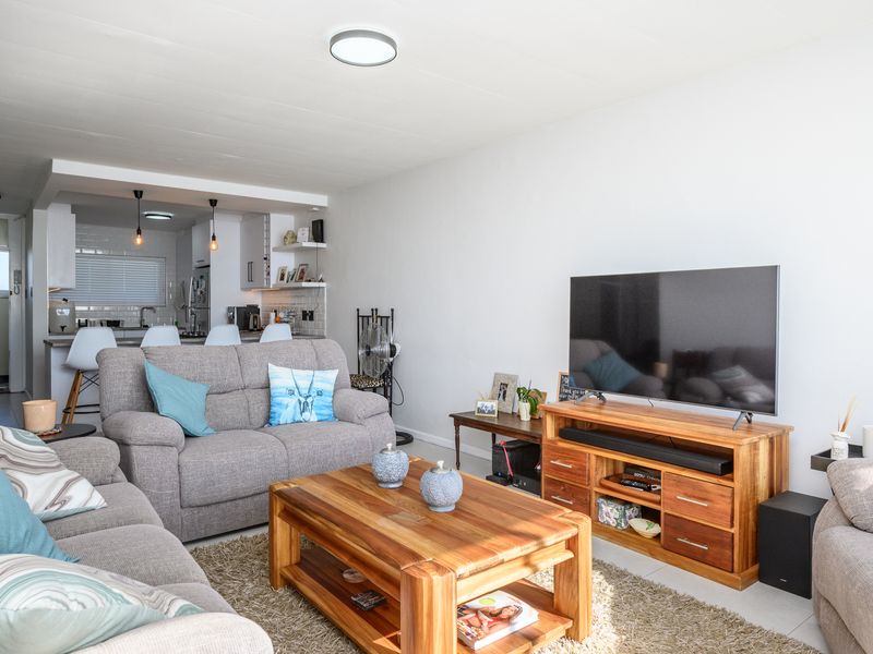 An open-plan living area featuring a comfortable lounge space flowing into a modern kitchen with subway tile backsplash and breakfast bar seating.