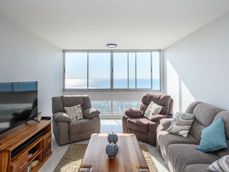 A bright living room featuring large sliding windows that offer expansive ocean views and provide ample natural light to the space.