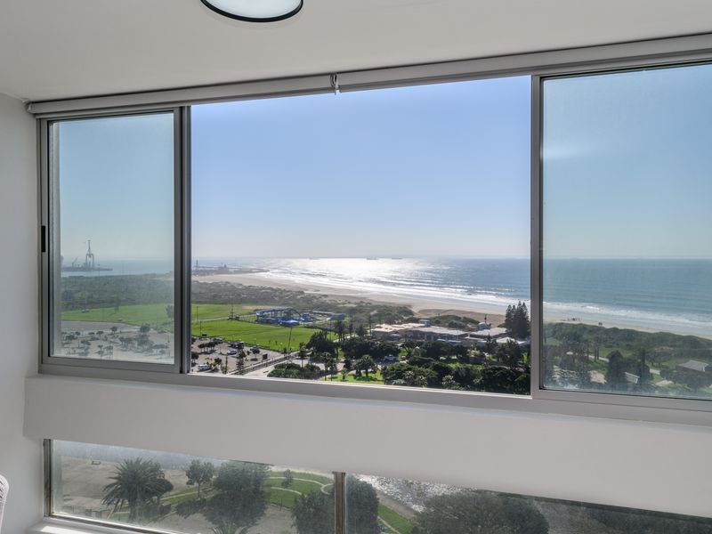 A bright interior space featuring large sliding windows that offer an expansive, elevated view of the coastline and ocean.