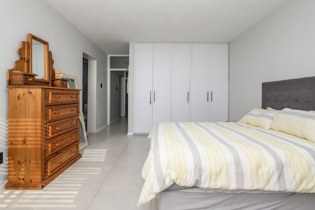A well-maintained bedroom featuring neutral tiled flooring and ample built-in cupboard storage, providing a clean and functional living space.