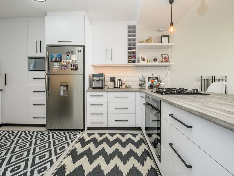 Modern kitchen featuring white cabinetry, subway tile backsplash, wood-look laminate countertops, and integrated gas hob and oven.