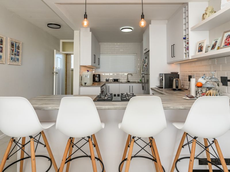 Modern kitchen featuring white cabinetry, subway tile backsplash, a central breakfast bar with an integrated gas hob, and stylish pendant lighting.