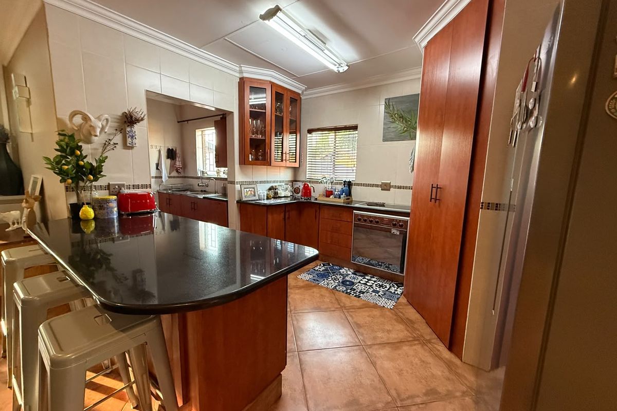 A functional kitchen featuring warm-toned wooden cabinetry, granite countertops, a central island with breakfast bar seating, and durable ceramic tile flooring.