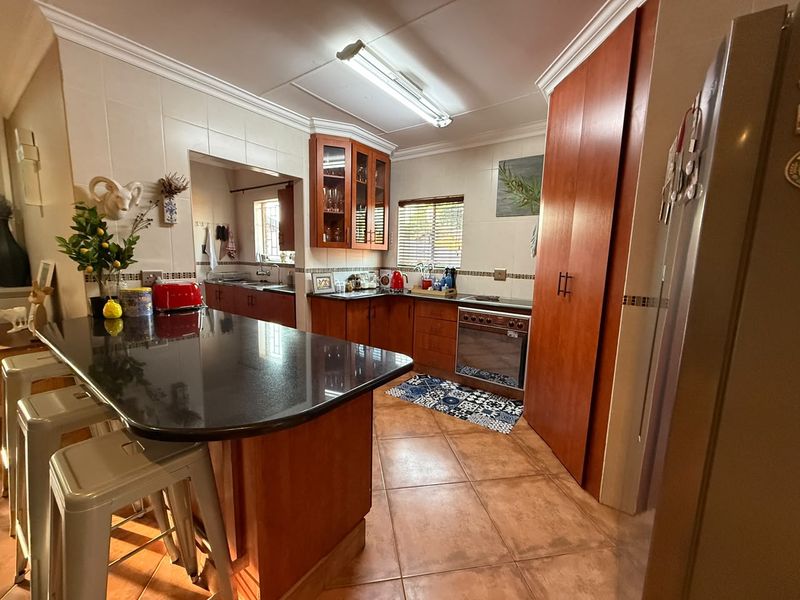 A functional kitchen featuring warm-toned wooden cabinetry, granite countertops, a central island with breakfast bar seating, and durable ceramic tile flooring.