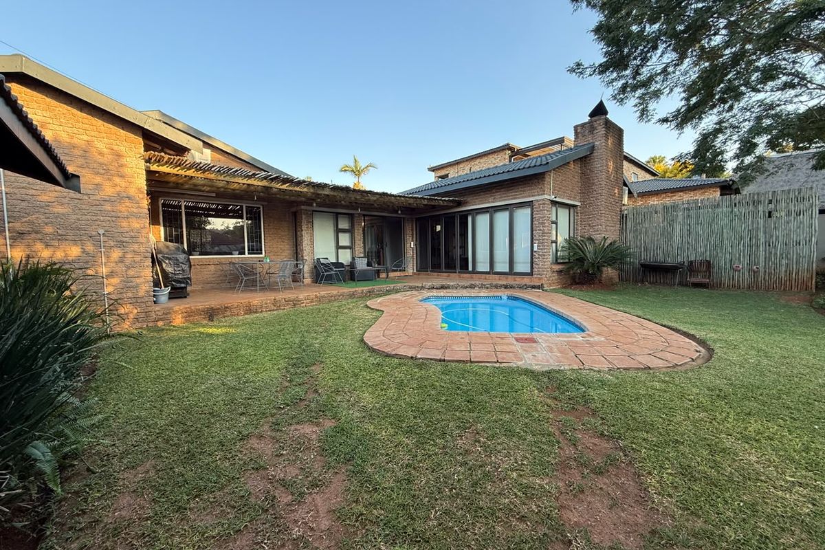 Rear exterior view featuring a swimming pool, brick-paved patio area, and covered outdoor space with brick facade and sliding glass doors.