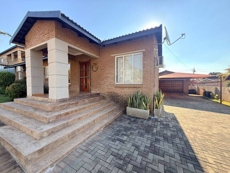 Front view of a brick house featuring a paved driveway, covered entrance porch with concrete steps, and an attached garage.