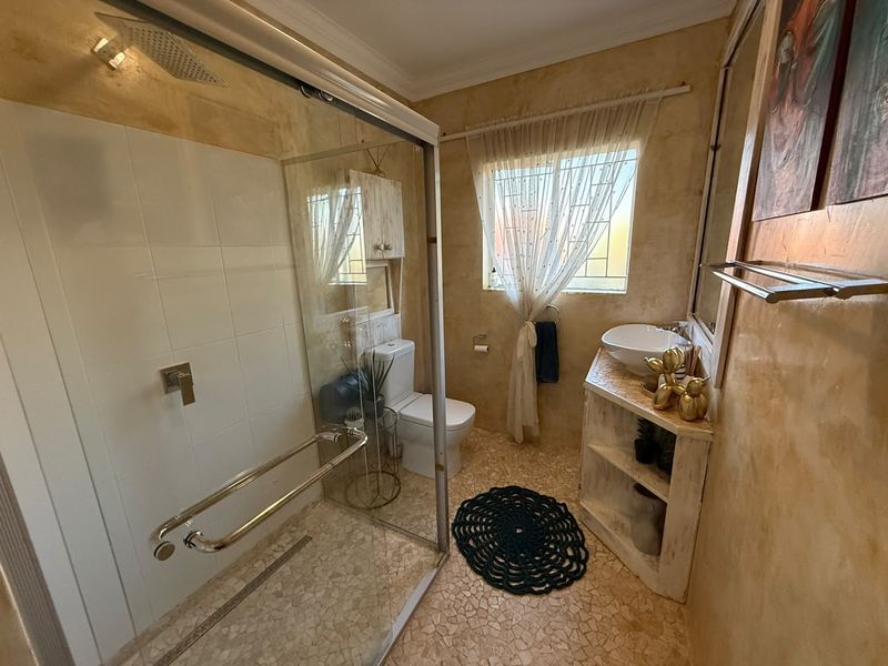 A compact bathroom featuring a glass-enclosed shower with a rain shower head, a vessel sink vanity, and textured wall finishes.