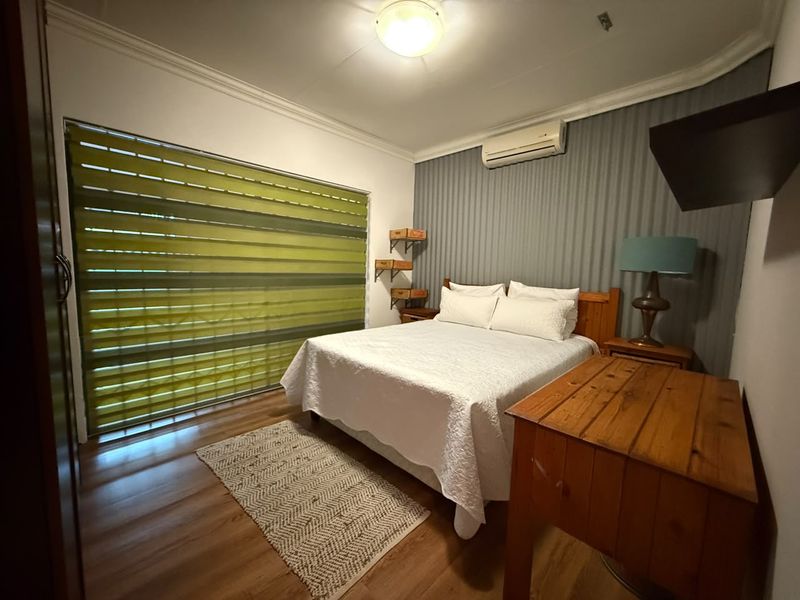 A cozy bedroom featuring laminate flooring, a textured feature wall, and a wall-mounted split-system air conditioner.