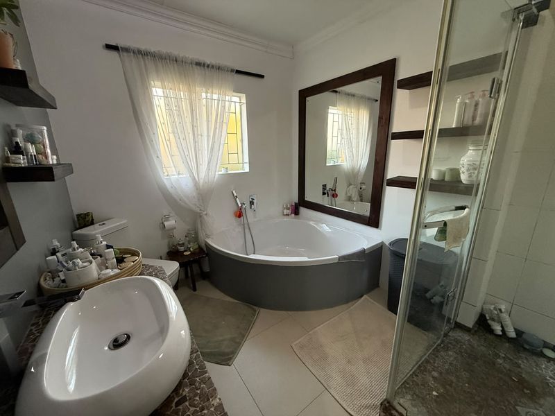 A functional bathroom featuring a corner bathtub, vessel sink with tiled vanity, glass shower enclosure, and built-in shelving for storage.