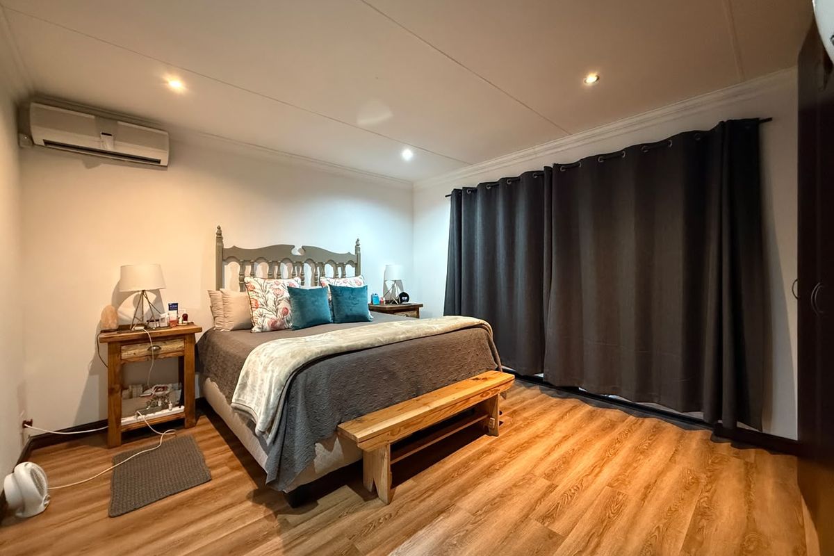 A well-maintained bedroom featuring laminate flooring, recessed downlighting, and a wall-mounted air conditioning unit.
