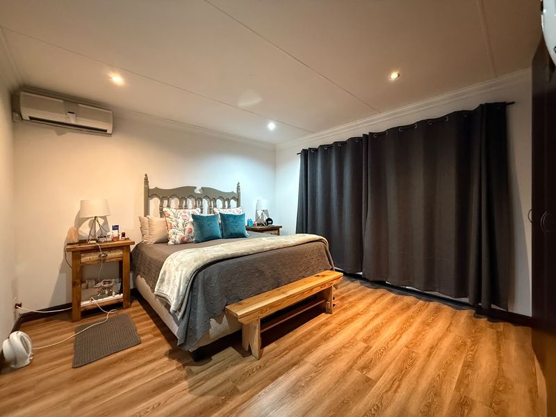 A well-maintained bedroom featuring laminate flooring, recessed downlighting, and a wall-mounted air conditioning unit.
