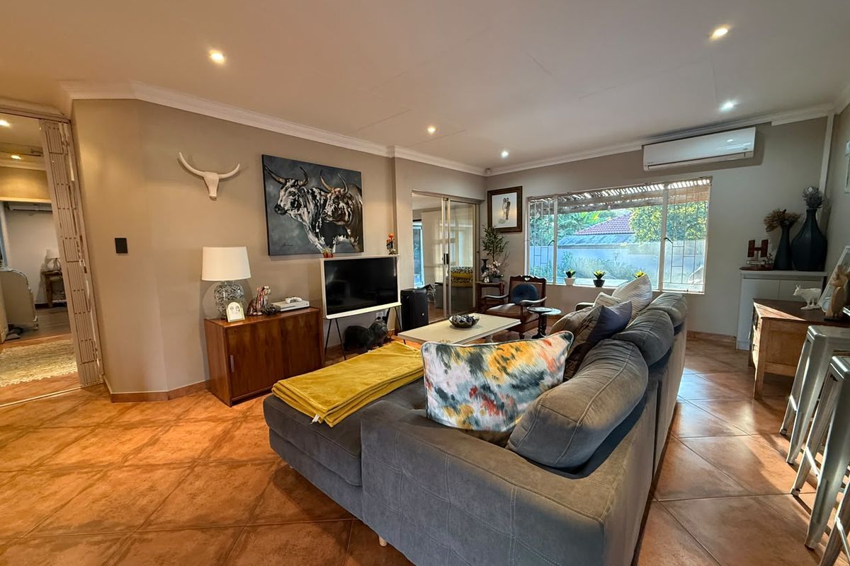 Spacious living room featuring terracotta floor tiles, recessed downlighting, and a wall-mounted air conditioning unit, with large windows providing natural light.