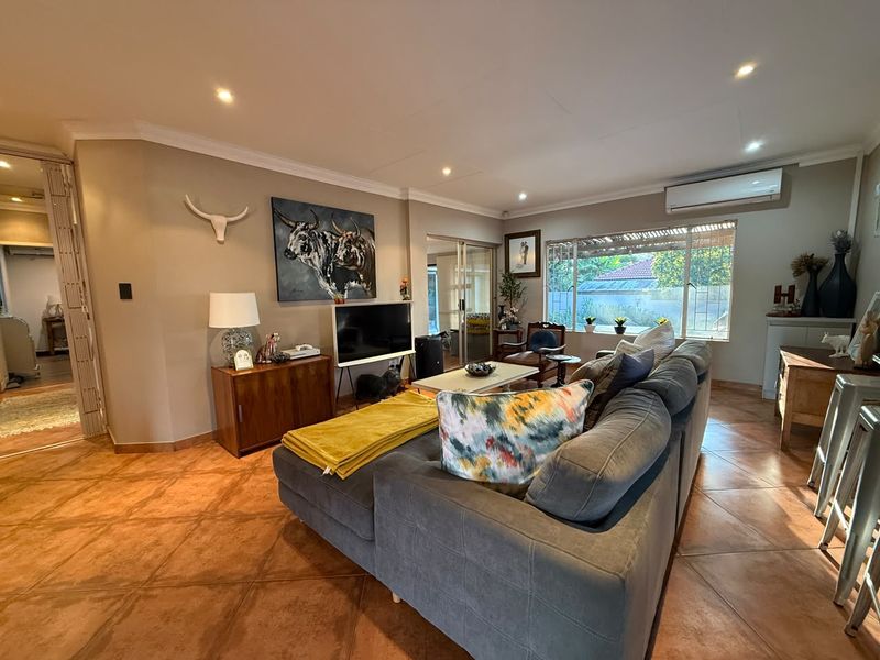 Spacious living room featuring terracotta floor tiles, recessed downlighting, and a wall-mounted air conditioning unit, with large windows providing natural light.