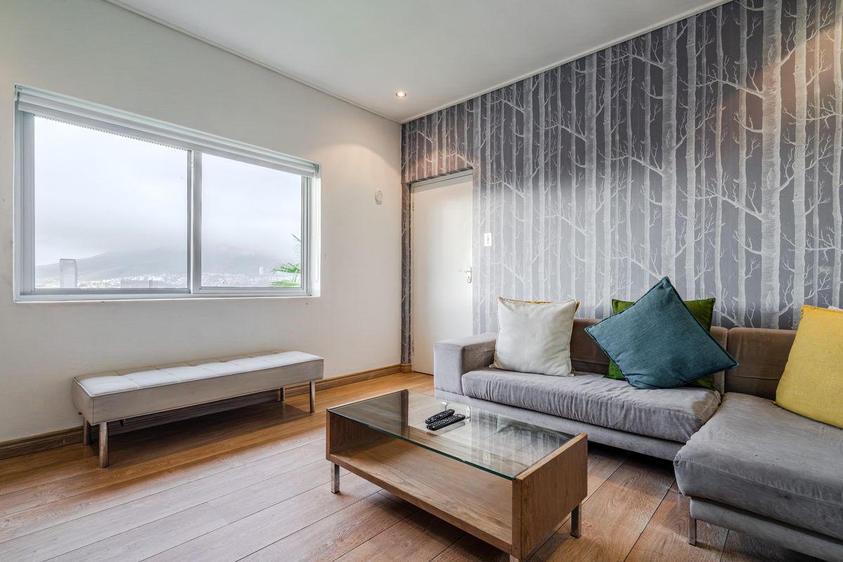 A bright living room featuring laminate flooring, recessed lighting, and a distinctive forest-themed feature wall, offering a comfortable and modern living space.