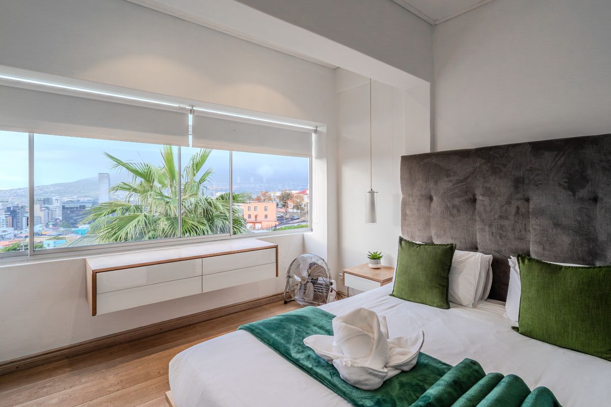 A bright bedroom featuring hardwood flooring, built-in floating cabinetry, and large windows offering expansive city views.