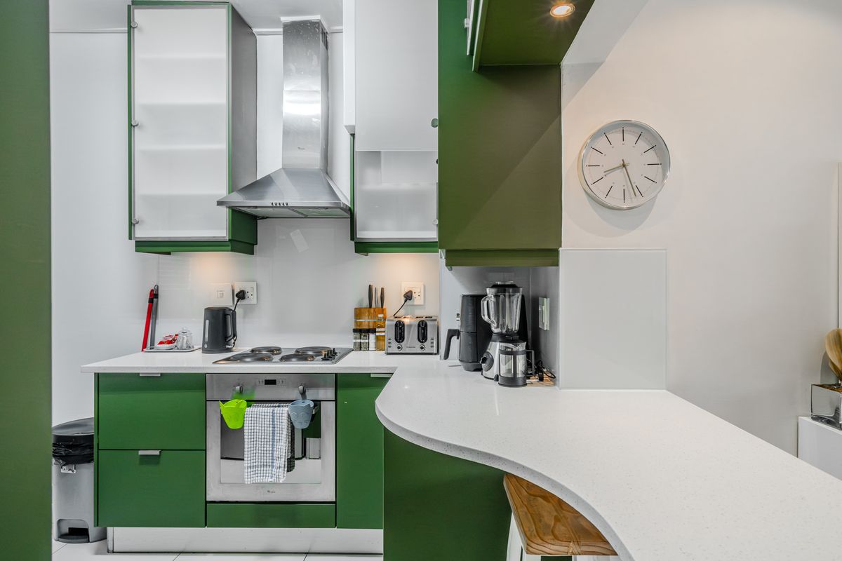 A modern kitchen featuring green cabinetry, white stone countertops, stainless steel appliances, and an integrated breakfast bar area.