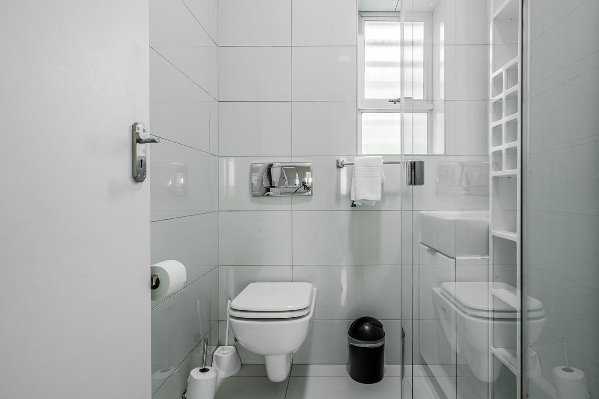 A modern, compact bathroom featuring a wall-mounted toilet with a concealed cistern, glass shower enclosure, and floor-to-ceiling white tiling.