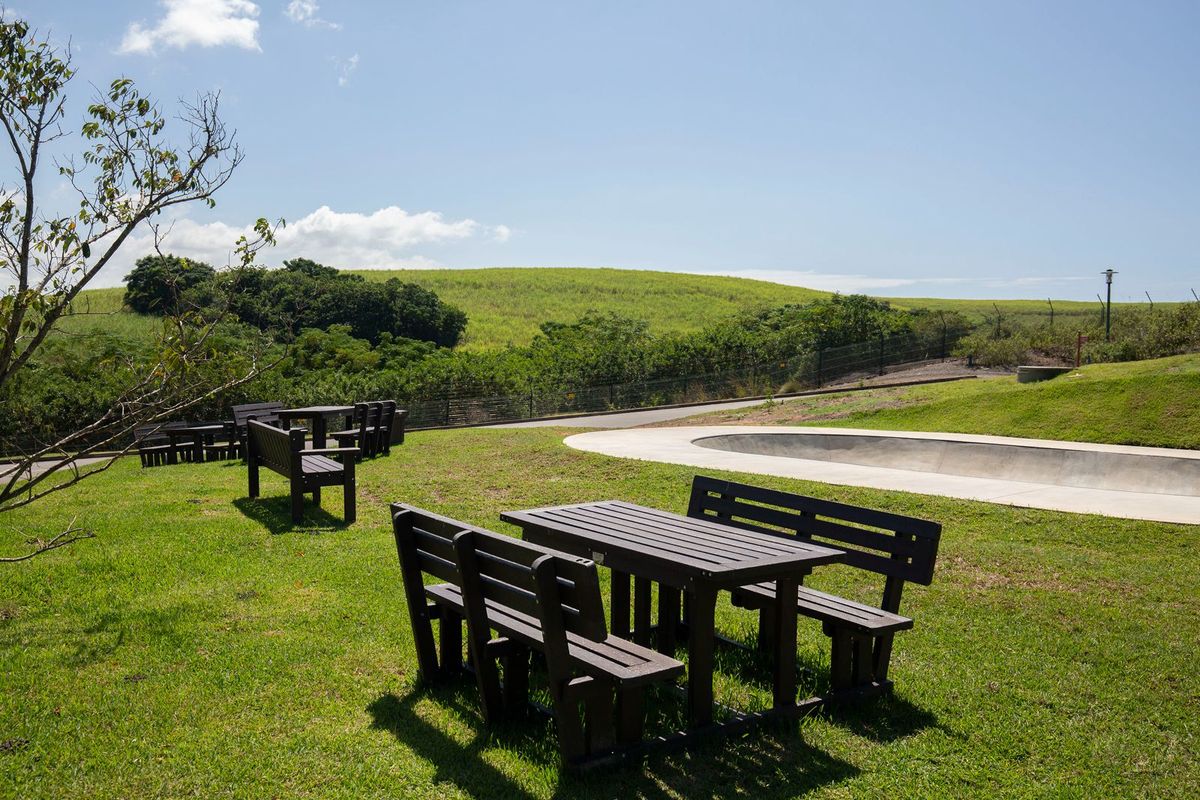 A well-maintained outdoor garden area featuring a concrete skate bowl, manicured lawn, and scenic hillside views.