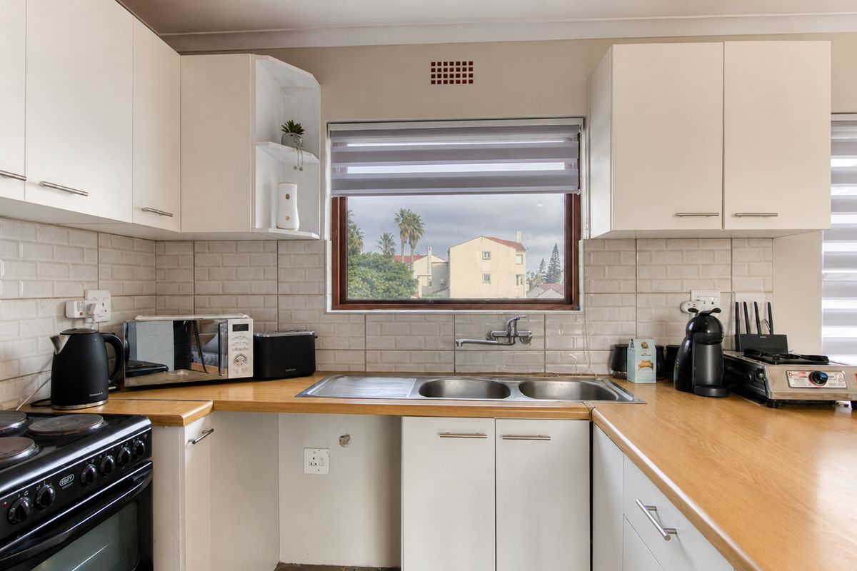 A functional kitchen featuring white cabinetry, wood-look laminate countertops, subway tile backsplash, and a double bowl stainless steel sink with a window view.