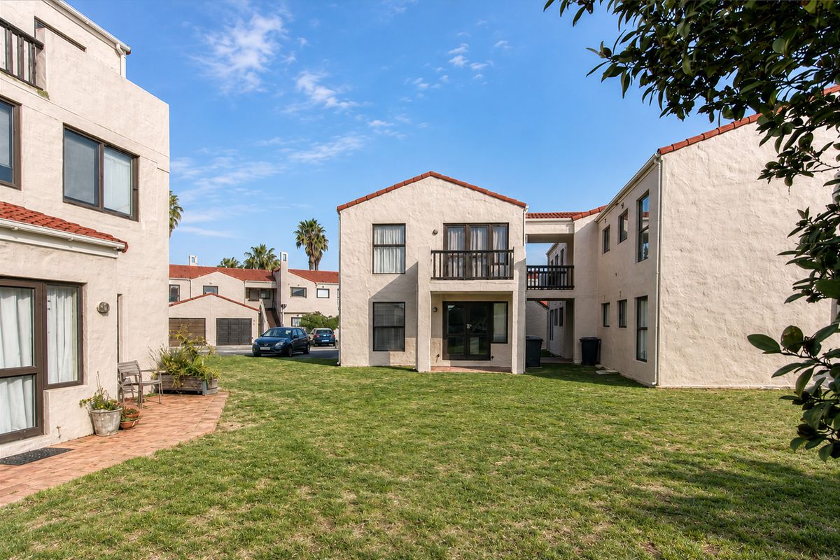 Rear view of a multi-story apartment complex featuring stucco facades, terracotta roof tiles, a shared lawn area, and private balconies.
