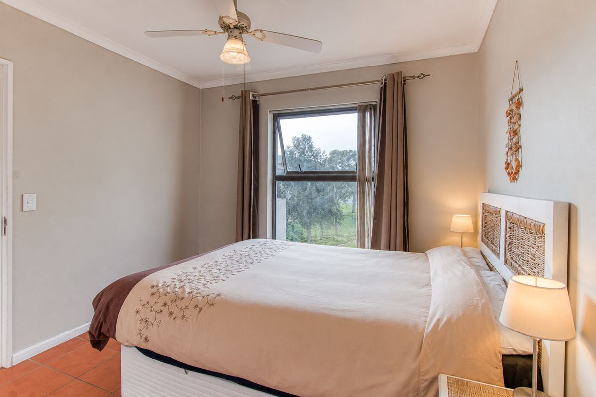 A cozy bedroom featuring tiled flooring, a ceiling fan, and a top-hung window providing natural light and exterior views.