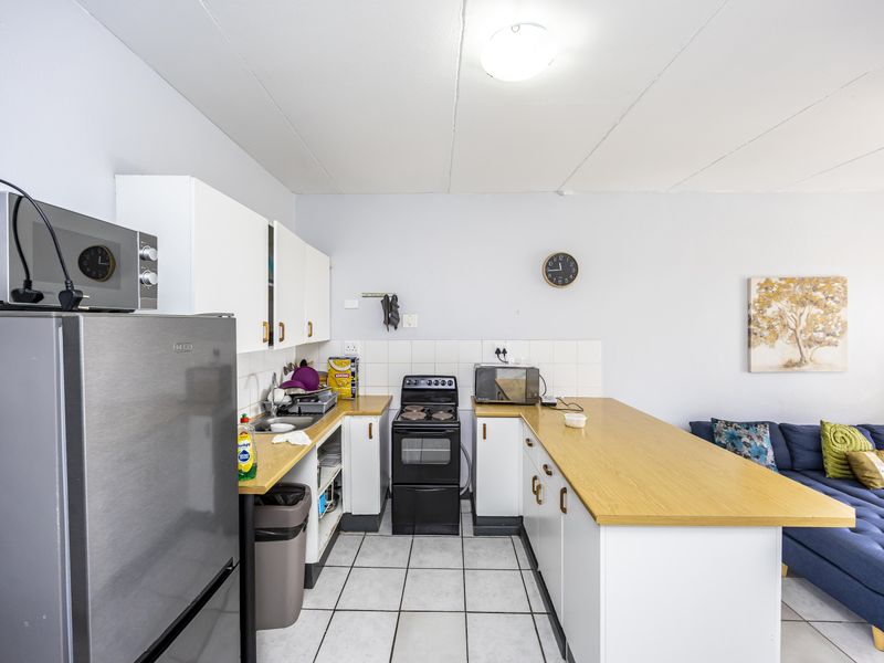 Open-plan kitchen featuring white cabinetry, laminate countertops, tiled backsplash, and a freestanding stove, seamlessly integrated with the adjacent living area.