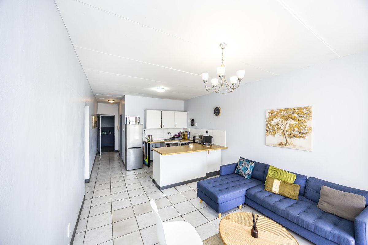 Open-plan living area featuring a functional kitchen with cabinetry and countertop, seamlessly flowing into the lounge space with tiled flooring throughout.
