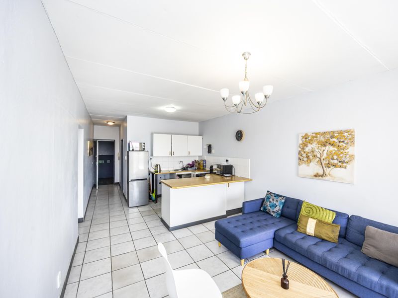 Open-plan living area featuring a functional kitchen with cabinetry and countertop, seamlessly flowing into the lounge space with tiled flooring throughout.